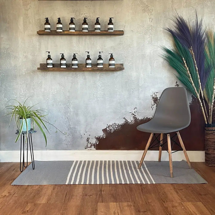 Gray eames-style chair with wooden legs and black frame on a striped grey and white indian cotton rug