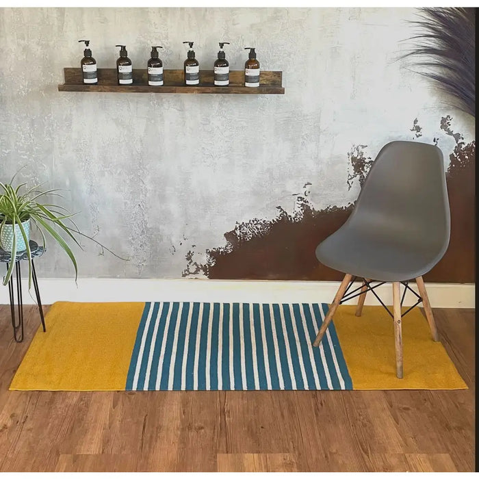 Gray molded plastic eames chair with light wood legs on a striped indian cotton rug in yellow and blue colors