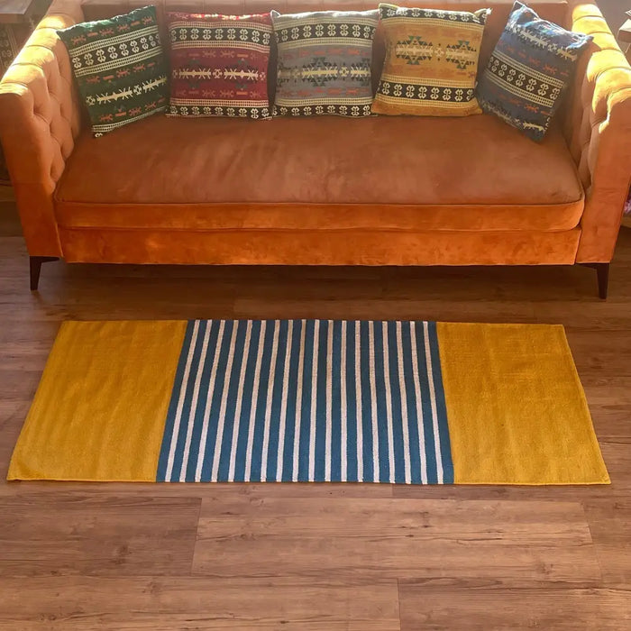 A rectangular indian cotton rug with mustard yellow sides and a central blue and white striped band woven textile