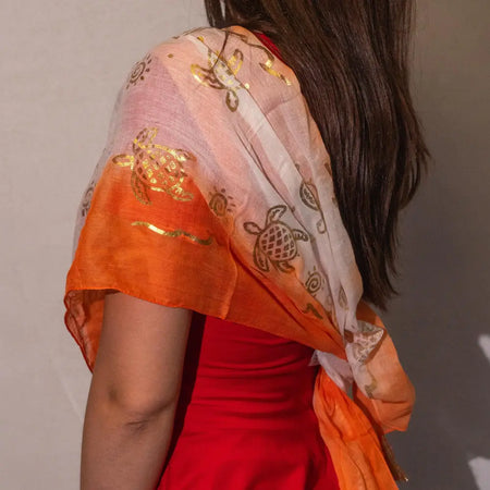 A sheer coral summer scarf with a gradient orange to white design and embroidered gold turtle prints