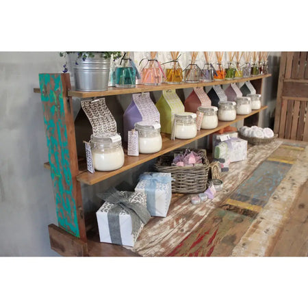 A rustic wooden shelf unit made of recycled wood displaying glass jars with white candles and decorative tags on a table