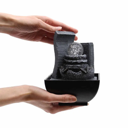 Black resin tabletop water feature with textured waterfall design and clear glass orb centerpiece