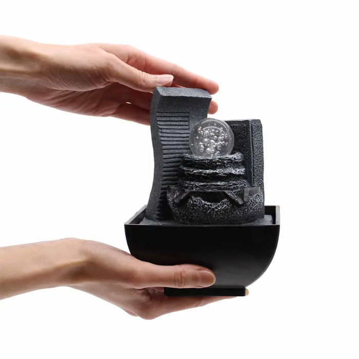 Black resin tabletop water feature with textured waterfall design and clear glass orb centerpiece