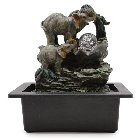 A tabletop water feature with gray elephant figurines and a glass sphere on a rocky base in a black rectangular basin