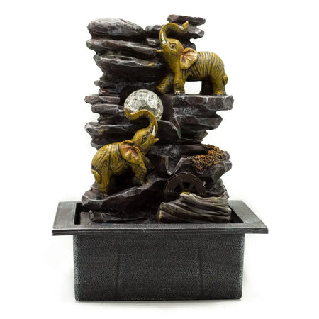 A tabletop water feature with two golden elephant figurines on dark rocks, featuring a water wheel and crystal ball