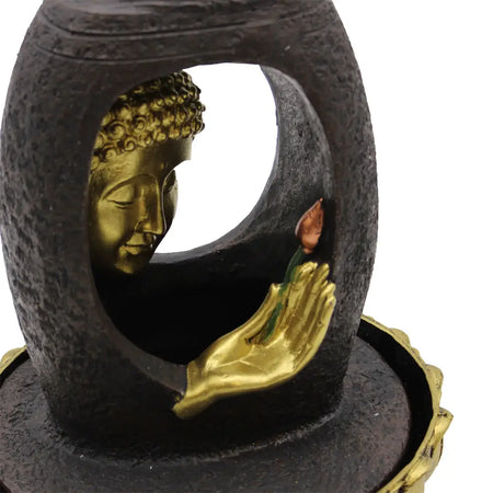 A golden buddha head and hand figurine in a dark stone frame as a tabletop water feature with vitarka mudra
