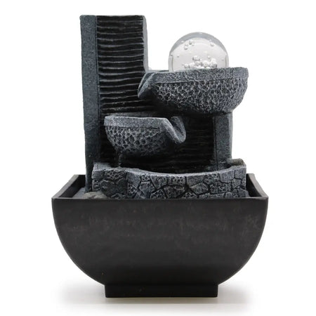 Black resin tabletop water feature with textured stone tiers and clear glass orb showing cascading water flow