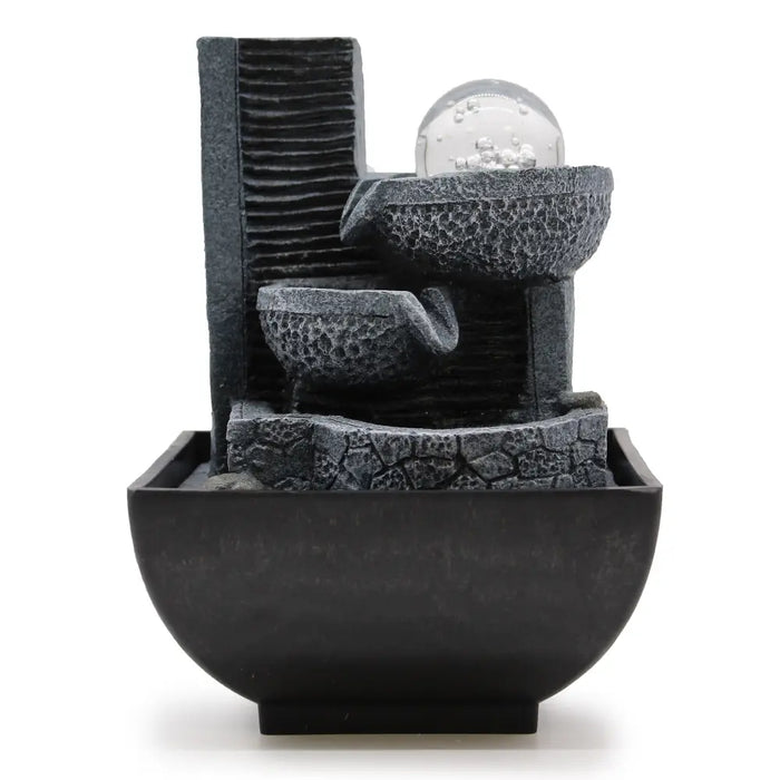 Black resin tabletop water feature with textured stone tiers and clear glass orb showing cascading water flow