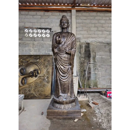 Bronze-colored antique gold standing buddha statue with intricate robes on a lotus base in an indoor workshop setting