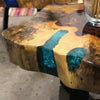 A tamarind wood coffee table with a rustic live edge and flowing turquoise resin inlays on a wooden floor