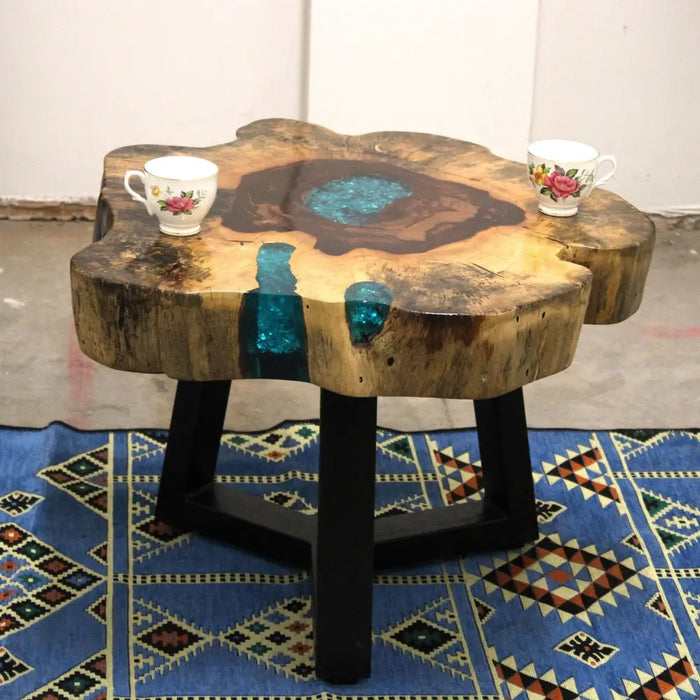 A rustic coffee table with a circular tamarind wood top featuring turquoise resin and black metal legs