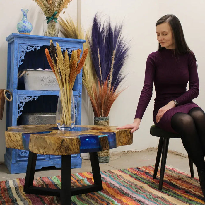 A round coffee table with tamarind wood top and sky blue resin inlay on black metal legs
