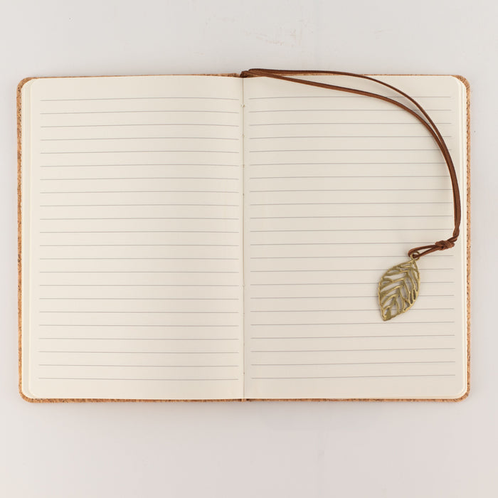 The Window, Milford Haven A5 notebook open to lined pages with a brass-coloured leaf bookmark on a cork effect cover.