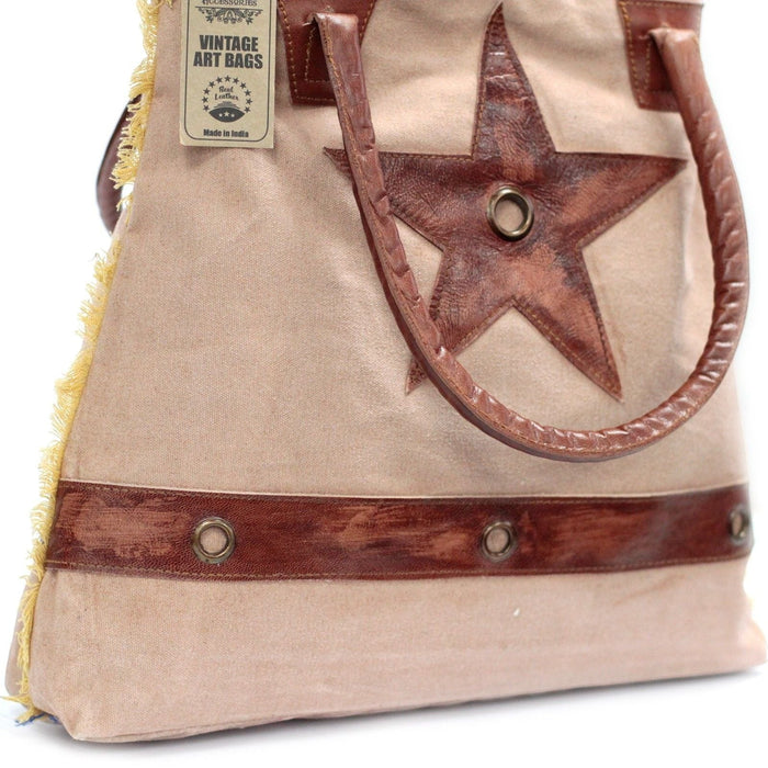 The Window, Milford Haven beige cotton tote bag with a brown leather star applique, leather handles, and frayed edges.