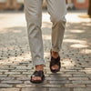 The Window, Milford Haven handmade dark brown leather sandals with crossed straps worn on a cobblestone street.