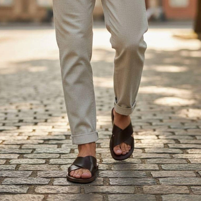 The Window, Milford Haven handmade dark brown leather sandals with crossed straps worn on a cobblestone street.