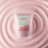 The Window, Milford Haven dusty rose scented candle sand in a pouch, surrounded by a swirl of loose pink wax beads.