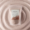 The Window, Milford Haven latte beige Pure Serenity candle sand in a pouch surrounded by a circular pattern of wax beads