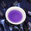 The Window, Milford Haven Libra zodiac fragrance oil in a white burner with purple glittery oil on blue satin fabric.