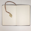 The Window, Milford Haven A5 notebook open to lined pages with a brass leaf bookmark on a leather-effect cover
