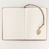 The Window, Milford Haven A5 notebook open to lined pages with a brass-coloured leaf bookmark on a brown leather cover