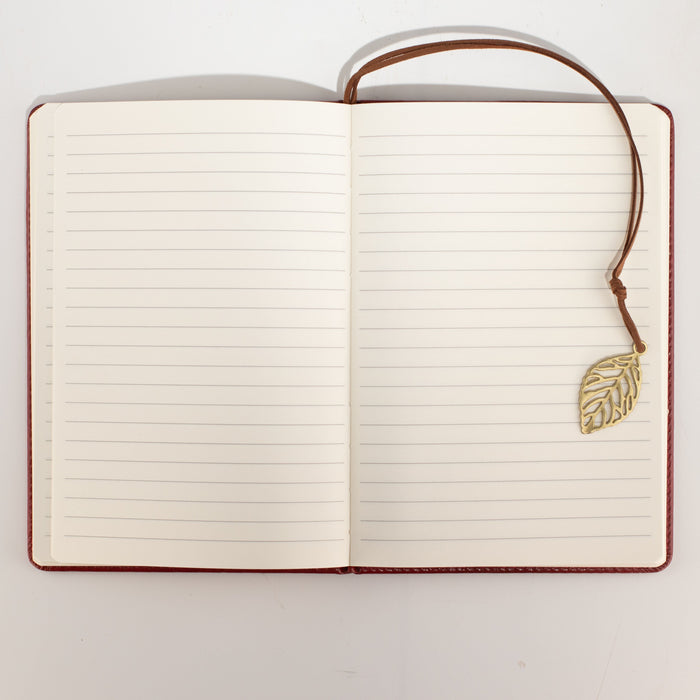 The Window, Milford Haven A5 notebook open to lined paper pages with a brass leaf bookmark on a red leather cover.