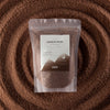 The Window, Milford Haven Crimson Crystal mocha brown candle sand in a 300g pouch surrounded by loose wax granules.