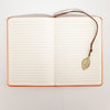 The Window, Milford Haven A5 notebook with lined paper pages and a brass-coloured leaf bookmark on an orange cover.