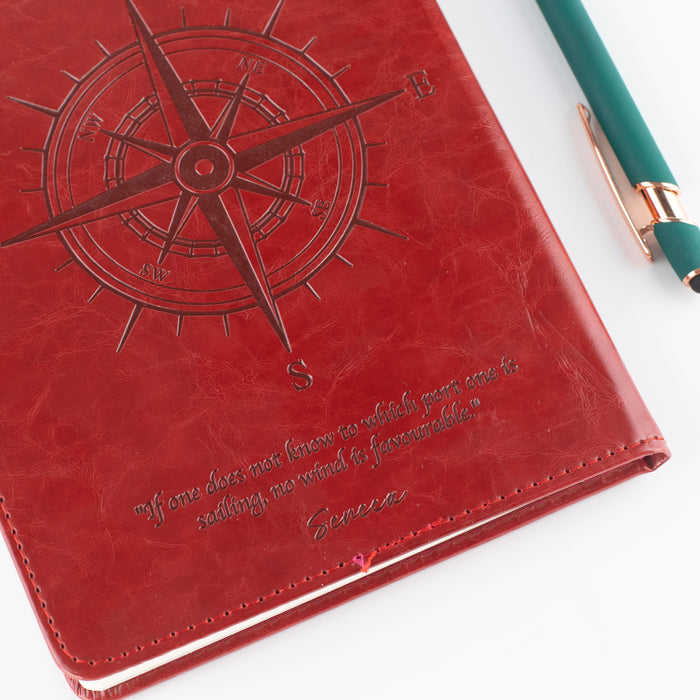 The Window, Milford Haven red leather-effect A5 notebook with an embossed compass design and a Seneca quote.