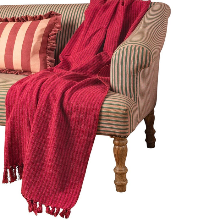 The Window, Milford Haven red and pink striped recycled cotton throw with tasselled fringes draped over a sofa.