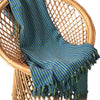 The Window, Milford Haven green and blue striped recycled cotton throw with tasselled fringe draped on a wicker chair.