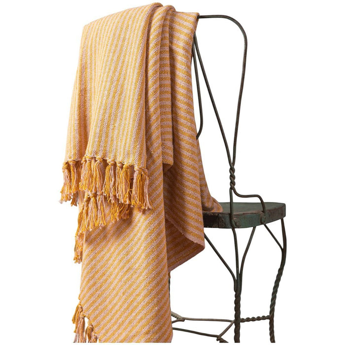 The Window, Milford Haven pale pink and mustard striped recycled cotton throw with tasselled fringe on a metal chair
