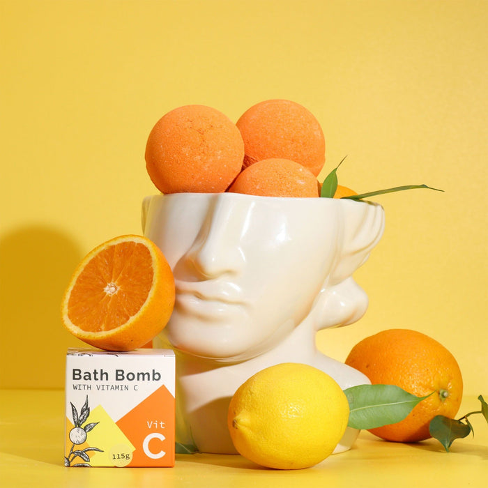 The Window, Milford Haven Vitamin C bath bomb in a white face-shaped bowl with fresh oranges and a lemon on yellow
