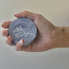 The Window, Milford Haven Wild Hare solid shampoo bar in purple with embossed logo held in a soapy hand