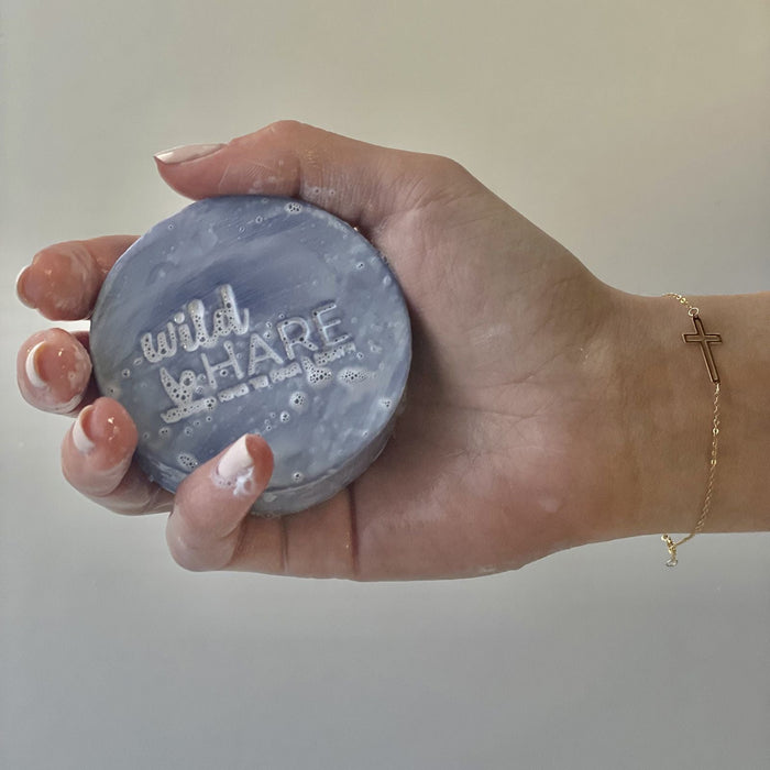 The Window, Milford Haven Wild Hare solid shampoo bar in purple with embossed logo held in a soapy hand