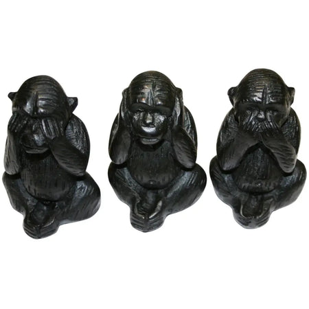 Three wise black wooden carved monkeys figurines showing see no evil hear no evil and speak no evil poses