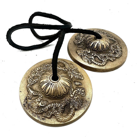 Pair of brass tibetan tingsha cymbals with dragon and floral embossing hanging on black leather cord