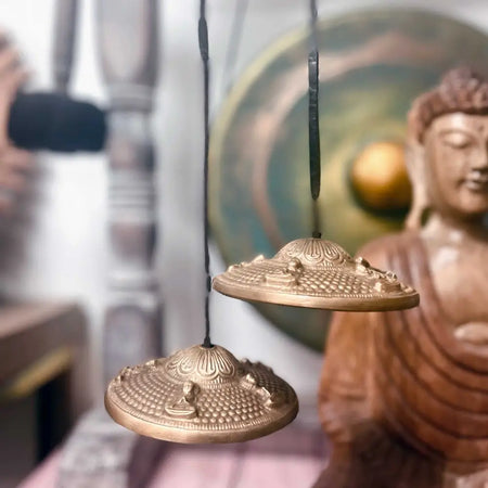 Two brass tingsha bells with chakra symbols engraved suspended by black cords for seven chakra meditation practices