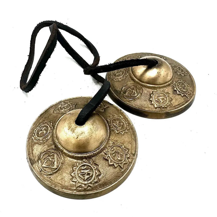 Pair of brass circular temple bells with intricate seven chakra symbols etched and hung on black leather cord