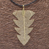 Gold tree leaf necklace with intricate mesh detailing on a leaf pendant hanging from a black cord