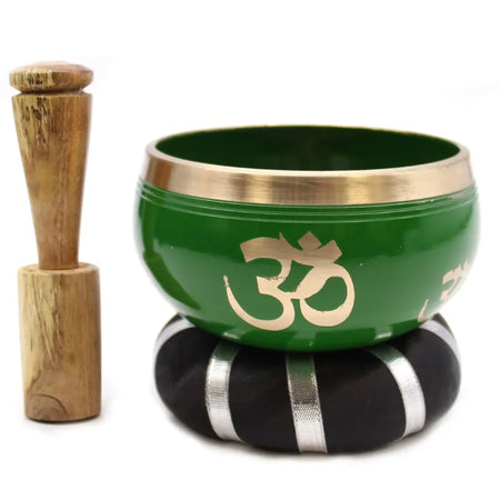 Green tibetan singing bowl set with gold om symbol and brass rim on black silver cushion next to wooden mallet
