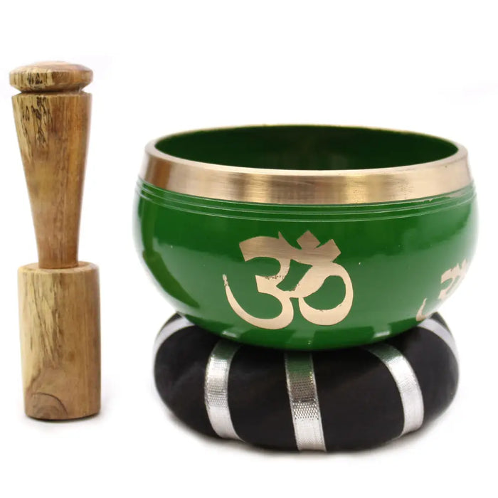 Green tibetan singing bowl set with gold om symbol and brass rim on black silver cushion next to wooden mallet
