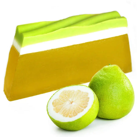 A layered green and yellow pomelo soap loaf with a white stripe shown next to whole and halved pomelos