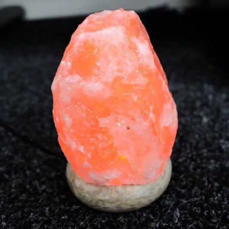 A glowing orange usb himalayan salt lamp with rough natural rock texture and smooth stone base showing hygroscopic properties