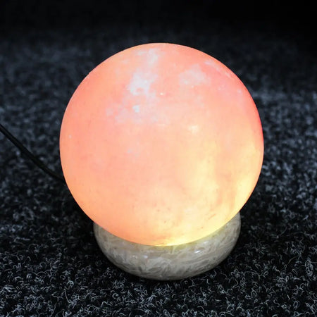 A glowing usb himalayan salt lamp ball with warm orange pink hue and natural mineral texture showing hygroscopic properties
