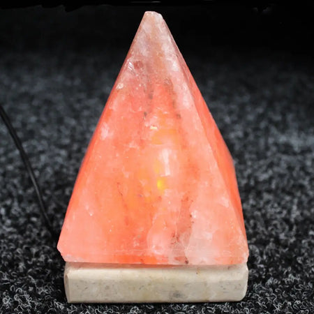 A usb himalayan salt lamp pyramid with a translucent peach crystalline surface and a white marble base showing hygroscopic properties