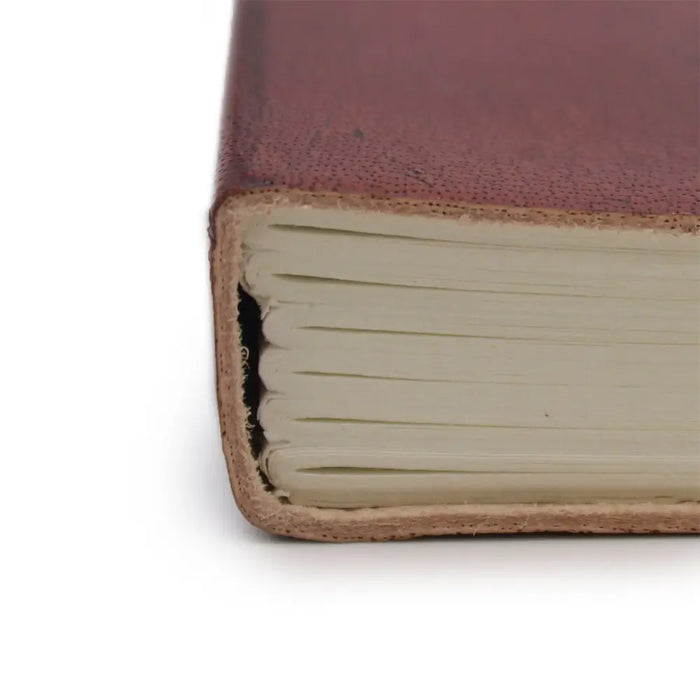 A rich burgundy vegetable tanned leather notebook with textured cover and neatly stacked off-white pages with strap