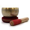Golden singing bowl with engraved sanskrit script resting on a red velvet cushion for singing bowl use 11cm