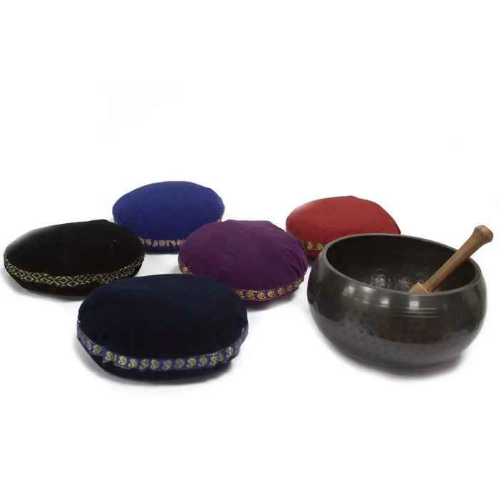 Dark hammered metal singing bowl with wooden mallet resting on a velvet singing bowl cushion 11cm