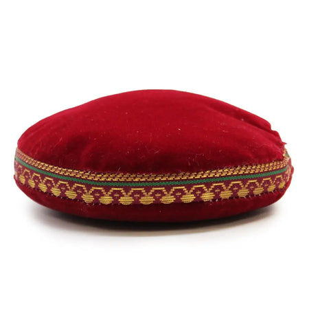 A plush round red velvet singing bowl cushion with gold and green woven decorative band, 11cm in size